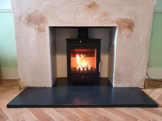 Woodburning stove in a plastered surround with a granite hearth
