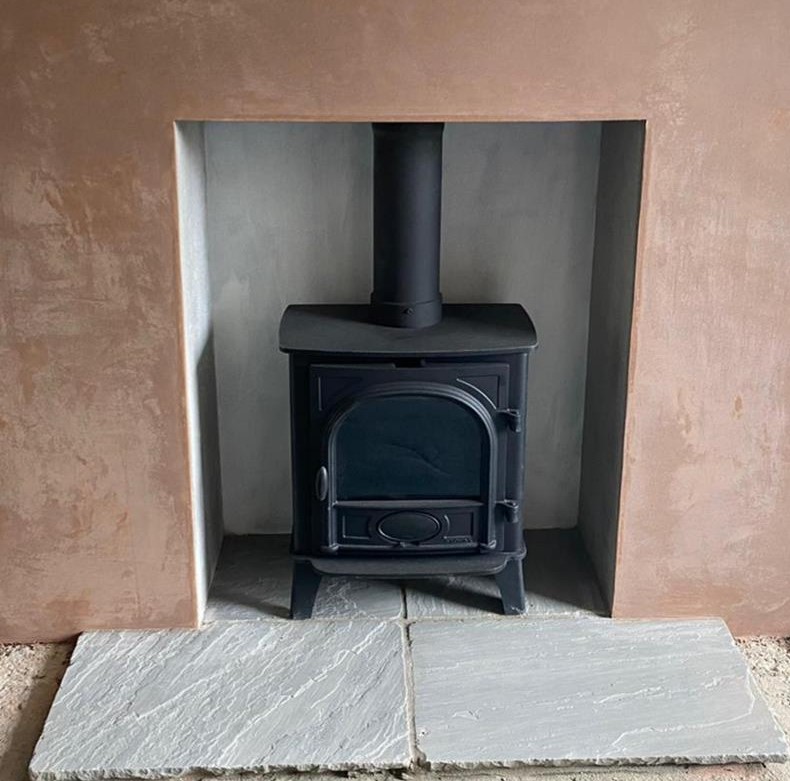 Sandstone flags hearth fitted to a woodburning stove in a plastered chimney breast.