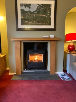 Woodburning stove fitted in a fireplace with wooden mantlepiece and slate hearth