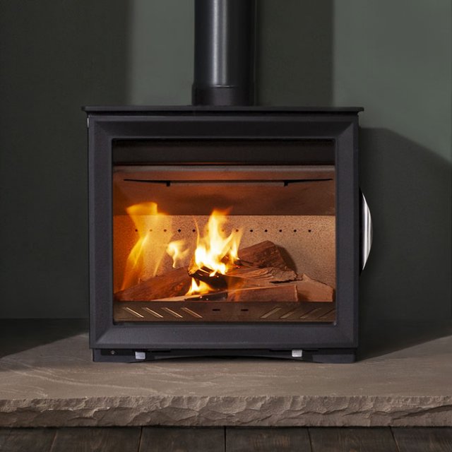 An Arada M-Series Wide Screen woodburning stove shown in a dark painted fireplace with burning logs inside.