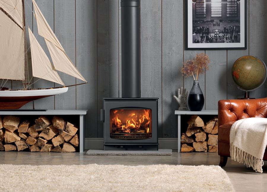 The Wychwood wood burning stove shown in a contemporary living room with logs stored either side.