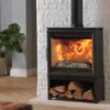A Charlton & Jenrick Woodtec 5XW wood burning stove shown next to a white painted wall with logs stored underneath.