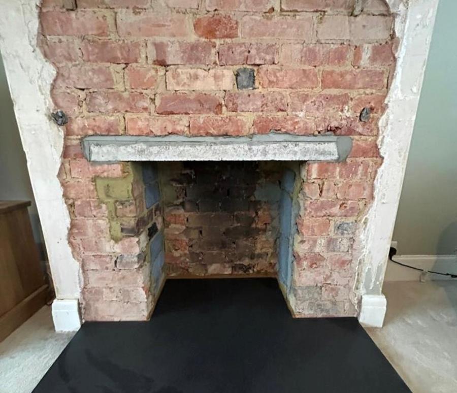 A bare brick fireplace with opening for woodburning stove