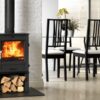 A freestanding multi fuel Charlton and Jenrick Fireline stove in a living room with dining table and chairs in the background. The stove has a log store underneath.
