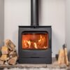 An Esse 775F woodburning stove shown lit in a fireplace with logs either side.