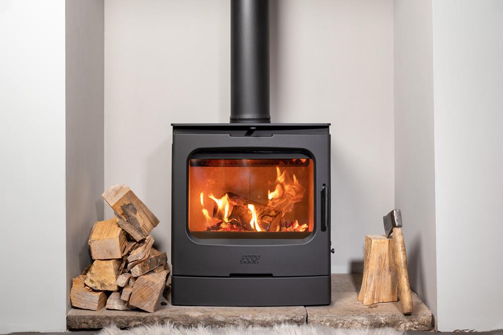 An Esse 775F woodburning stove shown lit in a fireplace with logs either side.