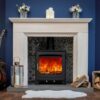 A Woodford Turing 5XL multifuel stove shown in a living room with a traditional stone fireplace, deep blue painted walls and a guitar leaning against the mantlepiece.