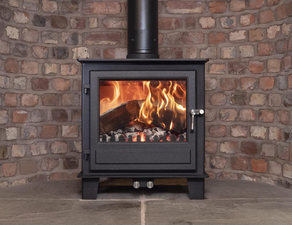 The Clock Blithfield multifuel stove shown in a fireplace with burning logs and brick hearth.