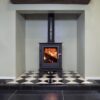 A compact multifuel stove shown in a chimney recess with wooden mantlepiece over.